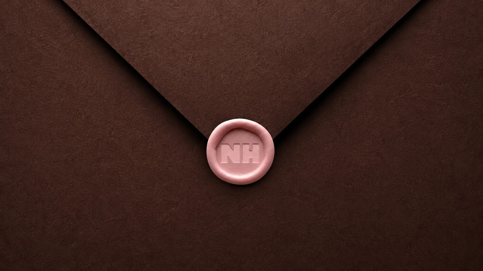 A pink wax seal stamped NH on a chocolate envelope